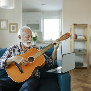 Elderly man learns to play acoustic guitar online using a Laptop