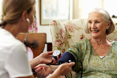 Happy senior woman's blood pressure being measured by caretaker in nursing home